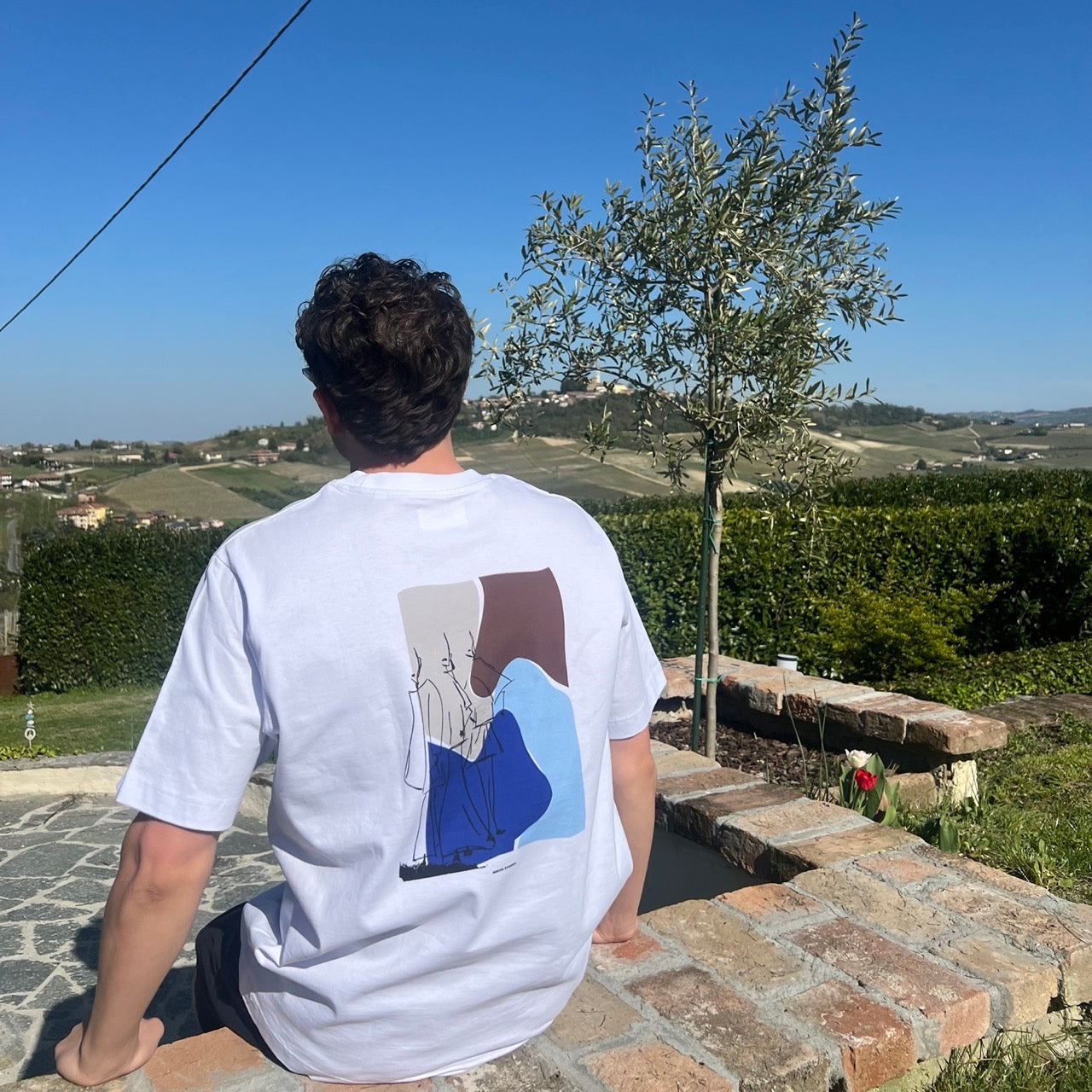 Persoon draagt wit Humae T-shirt van Nouve Studios met grote rugprint in een outdoor setting
