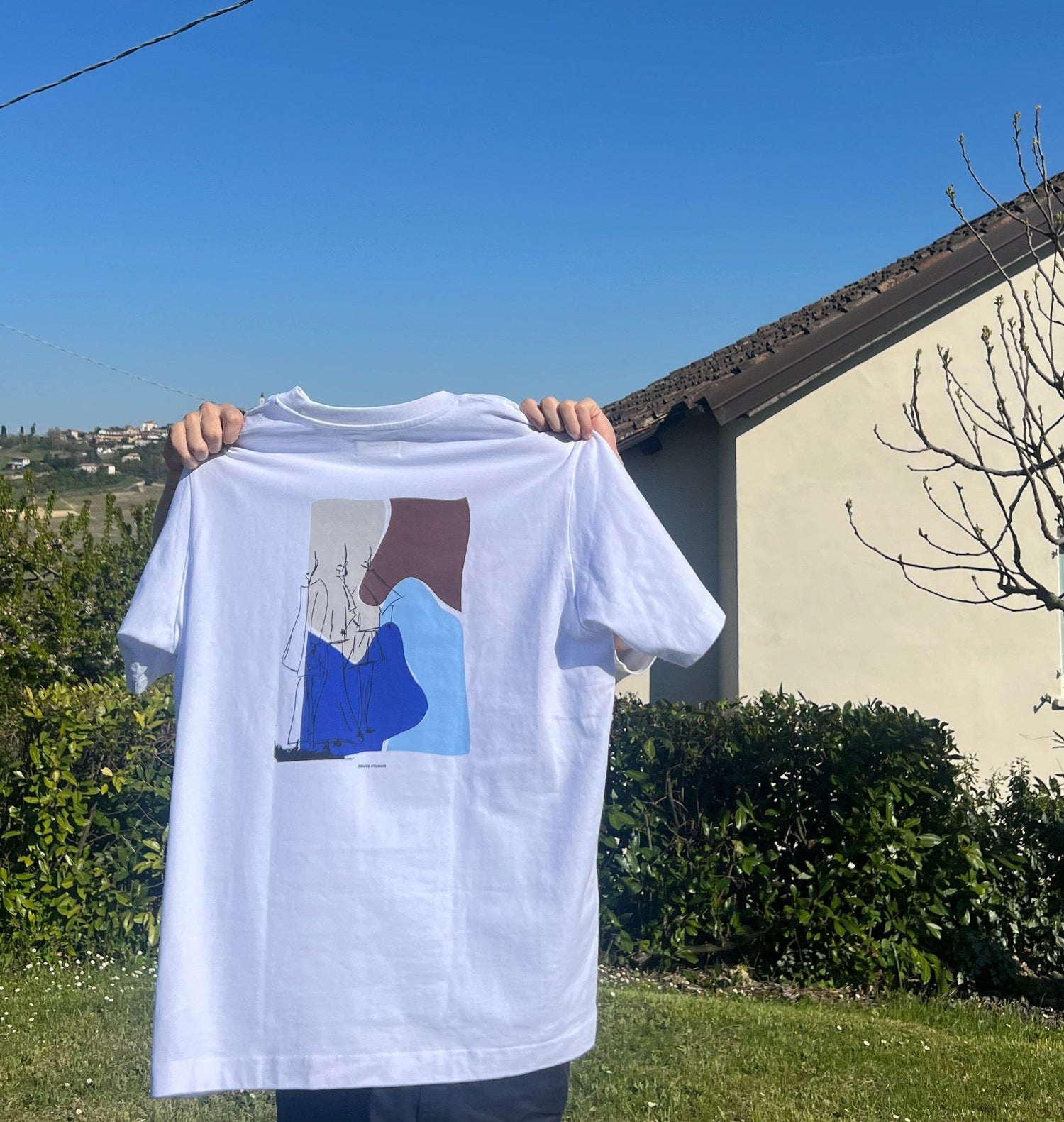 Persoon draagt wit Humae T-shirt van Nouve Studios met grote rugprint in een outdoor setting